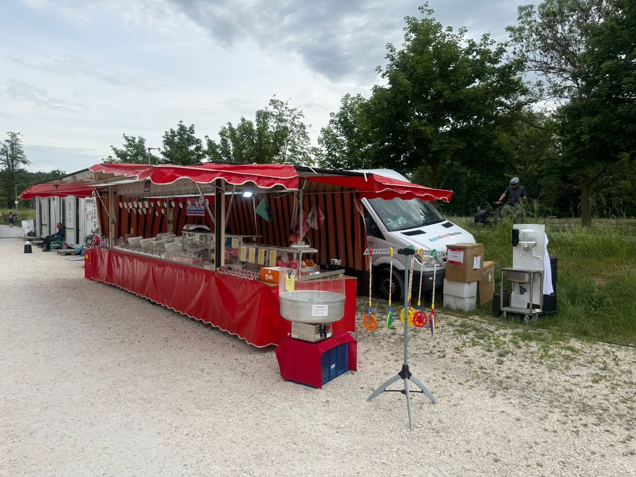 Roter Süßwarenstand mit Markise, davor eine Zuckerwatte-Maschine